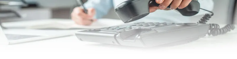 Person answering a corded telephone while taking notes.