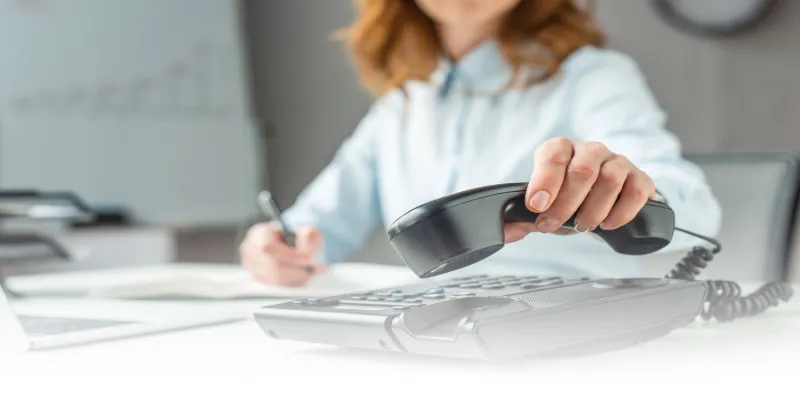 Person answering a corded telephone while taking notes.